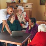 Caregiver showing seniors something on a laptop during a home sharing program in Vancouver