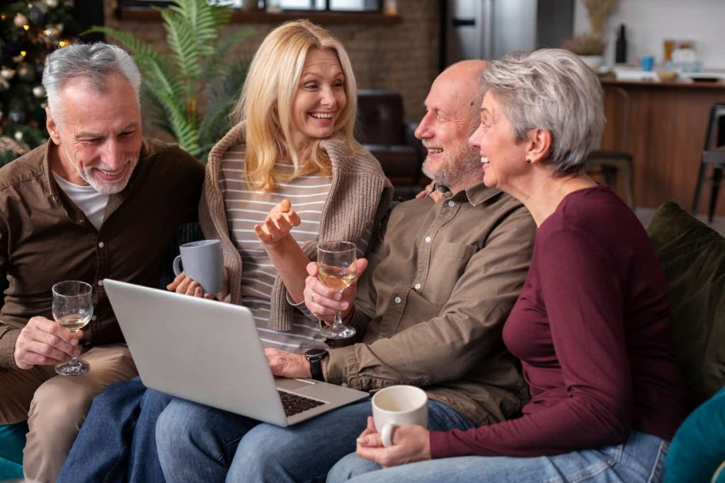 Group of smiling older adults sitting together on a couch, talking and using a laptop, representing community and supportive home sharing in Vancouver.